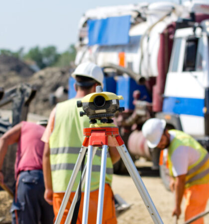 Theodolite on tripod at road construction site with workers supervising works